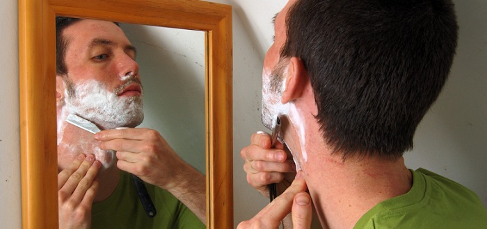 a young man shaving and looking in a mirror