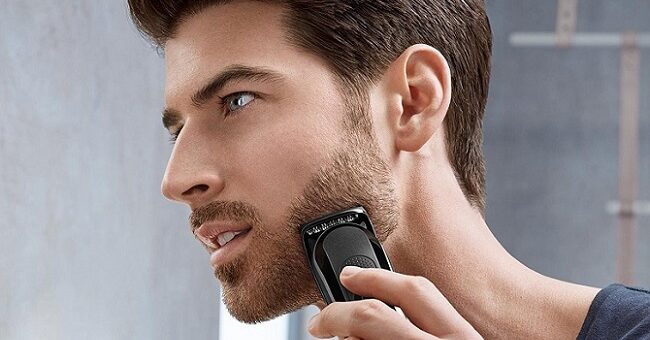 a young attractive man using a grooming machine to trim his beard