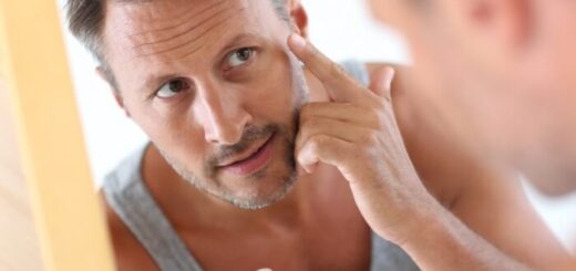 man in bathroom applying skin care product on face in the mirror