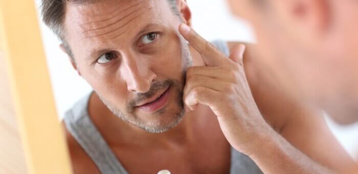 man in bathroom applying skin care product on face in the mirror