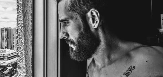 black and white of a tattooed man with beard looking through the window