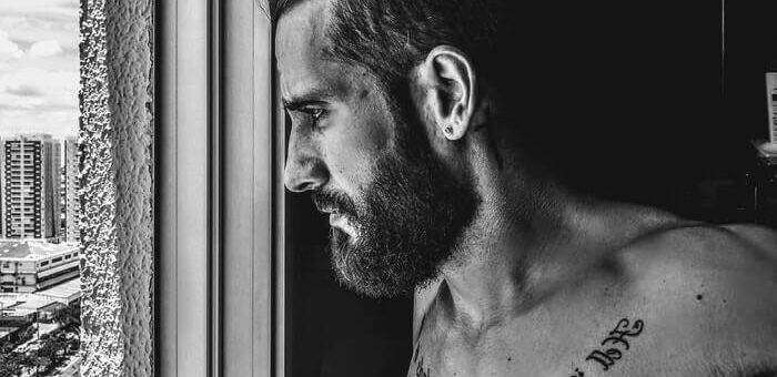 black and white of a tattooed man with beard looking through the window