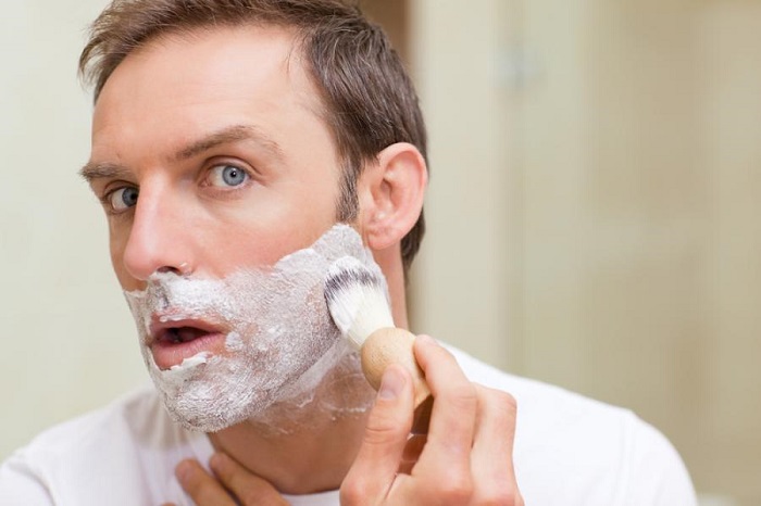 man in the bathroom applies shaving soap foam on face with shaving brush
